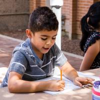 A young boy writing in a journal outside. 