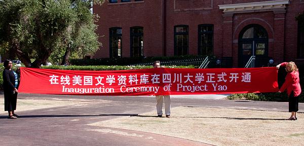 Acting department chair Maureen Daly Goggin (right), Joe Lockard (middle), and Demetria Baker (left) hold up a banner from the inauguration ceremony for Project Yao held at Sichuan University in China.