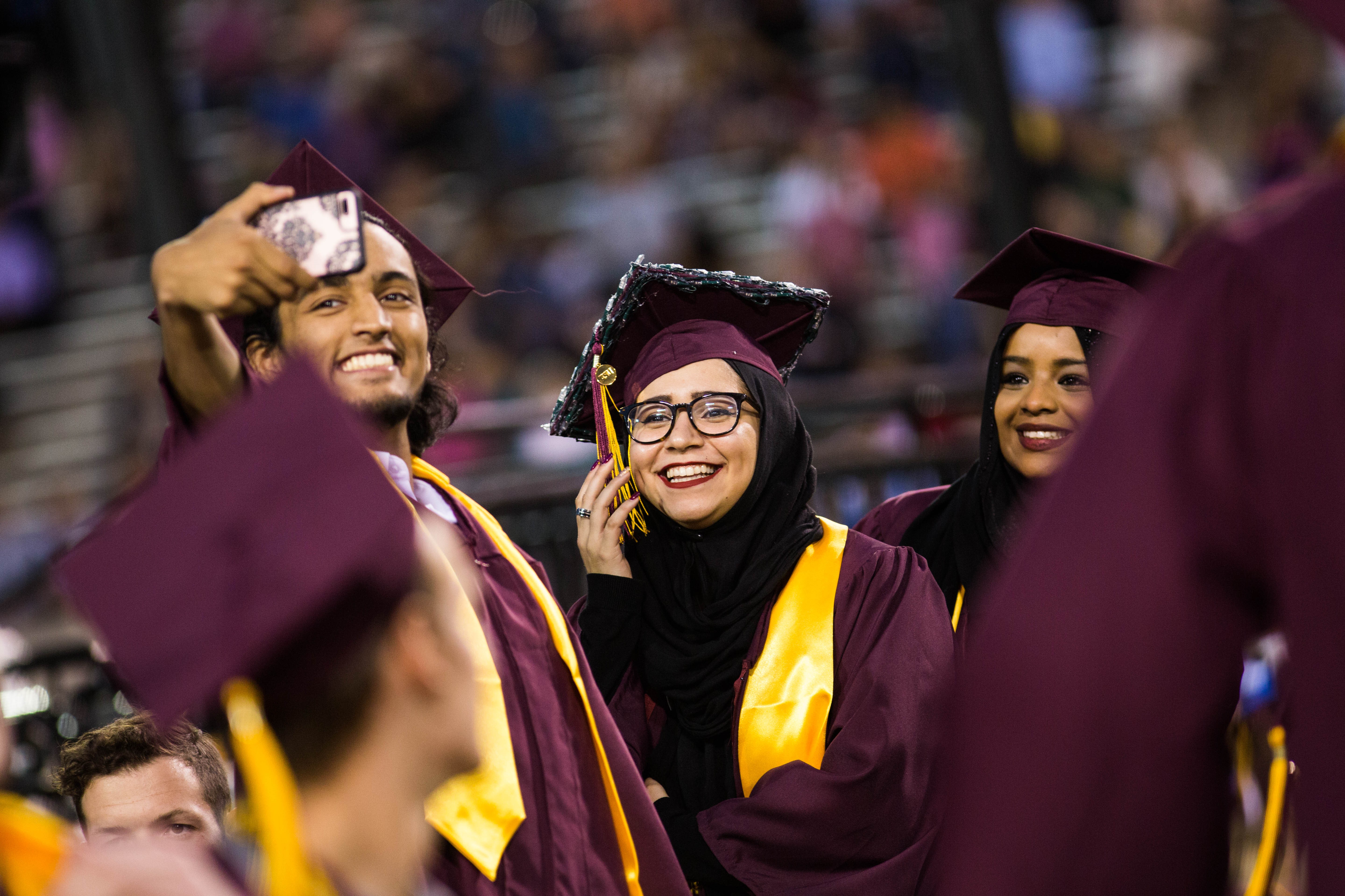 Three students wearing graduation regalia, smiling and taking a selfie.