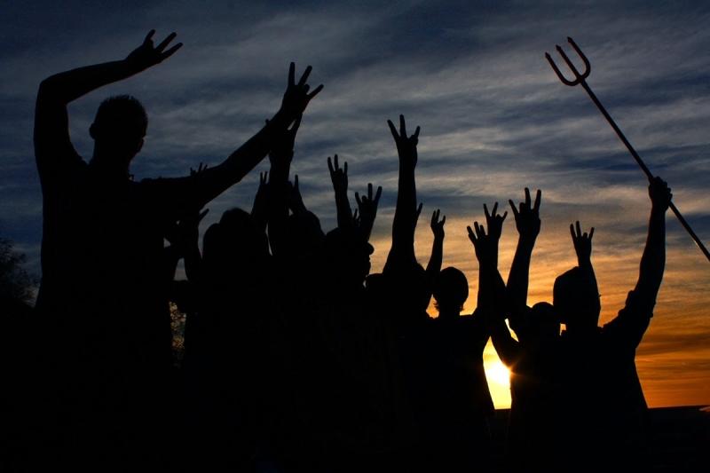 A silhouette of ASU Sun Devils making the pitchfork salute at sunset.